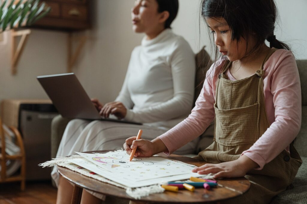 Mother balancing work life from home and daughter drawing beside.