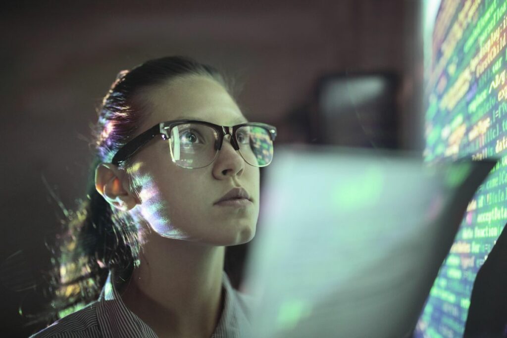 Female data compression engineer wearing glasses and looking at coding on monitor.