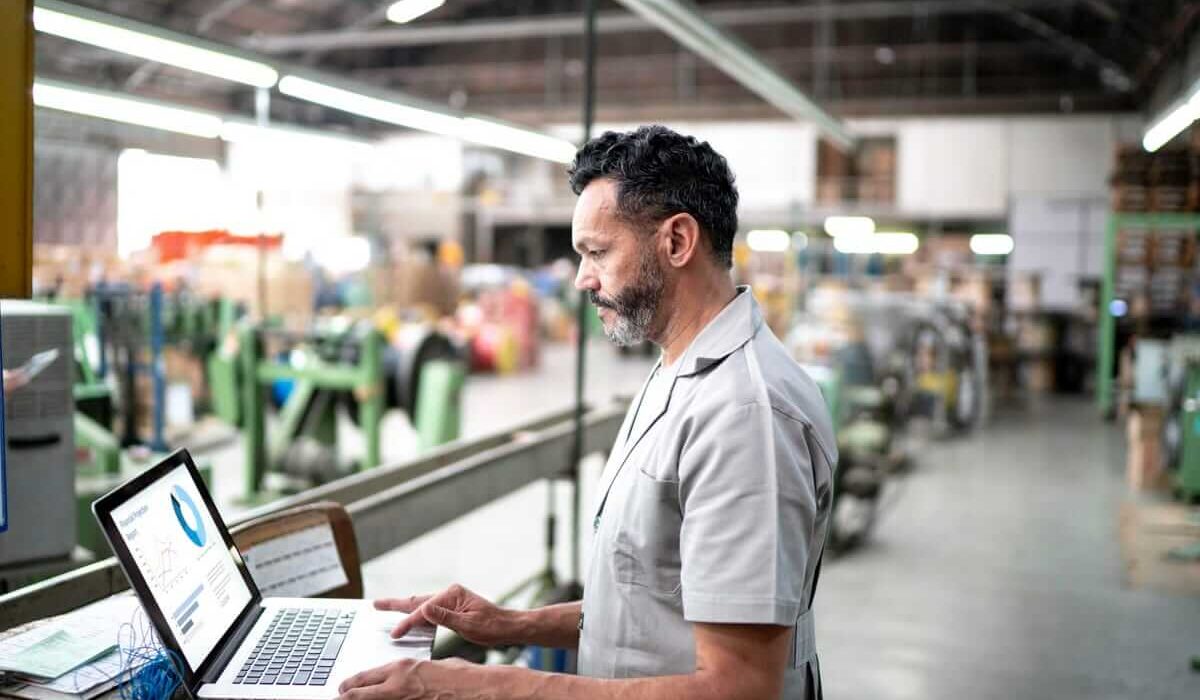 A man standing and working on computer to optimize supply chain integration in factory